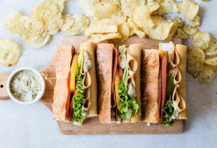 Plant-based sub sandwich on cutting board with chips