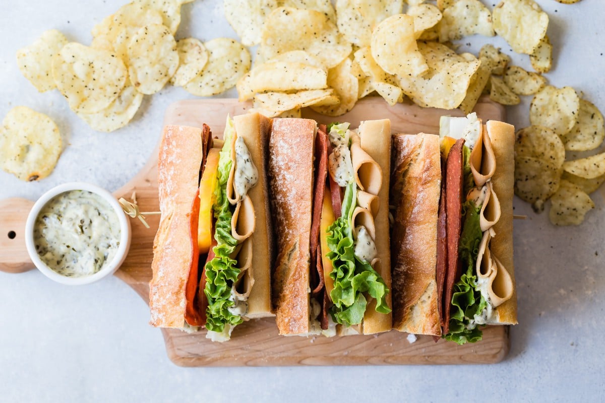 Plant-based sub sandwich on cutting board with chips