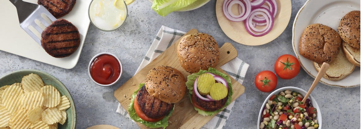 Plant-based burgers on cutting board with chips and condiments