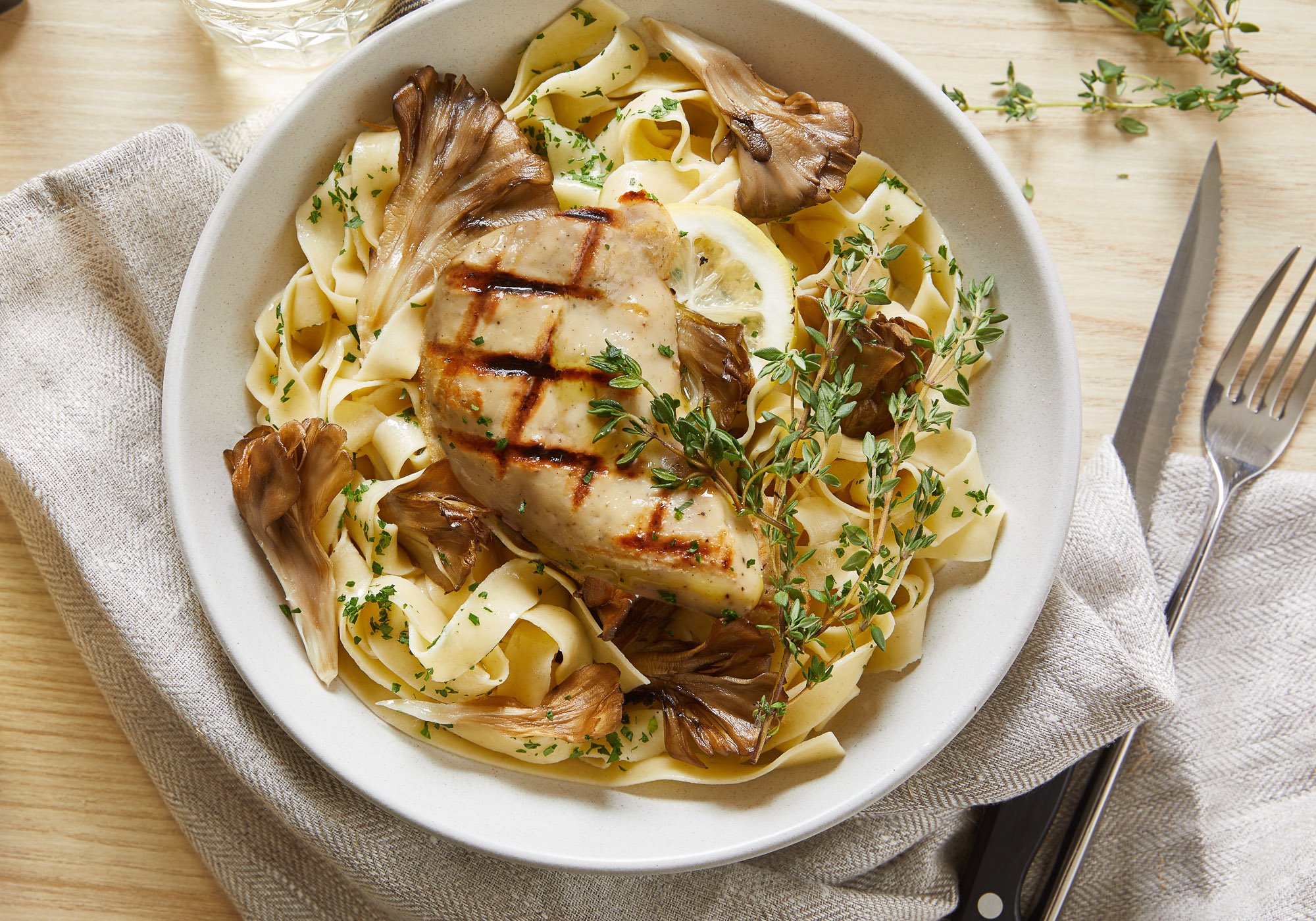 Cultivated grilled chicken on a bed of mushroom pasta and herbs viewed from above