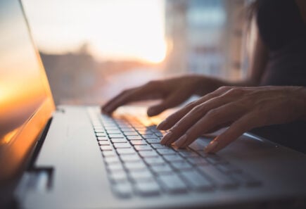 Hands typing on a laptop computer keyboard, representing mooc concept for cultured meat and plant-based meat science.