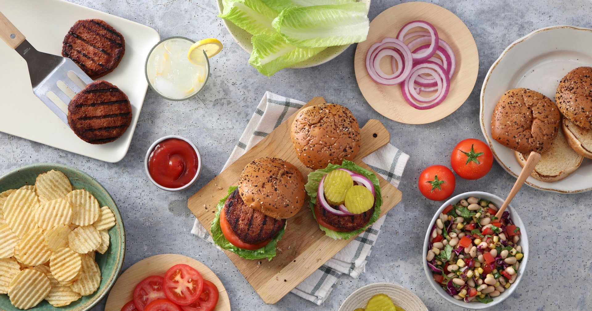 Burgers with toppings, chips, and bean salad