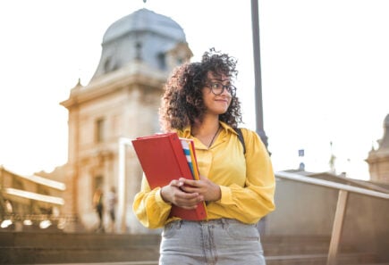 A student walking with notebooks on a college campus