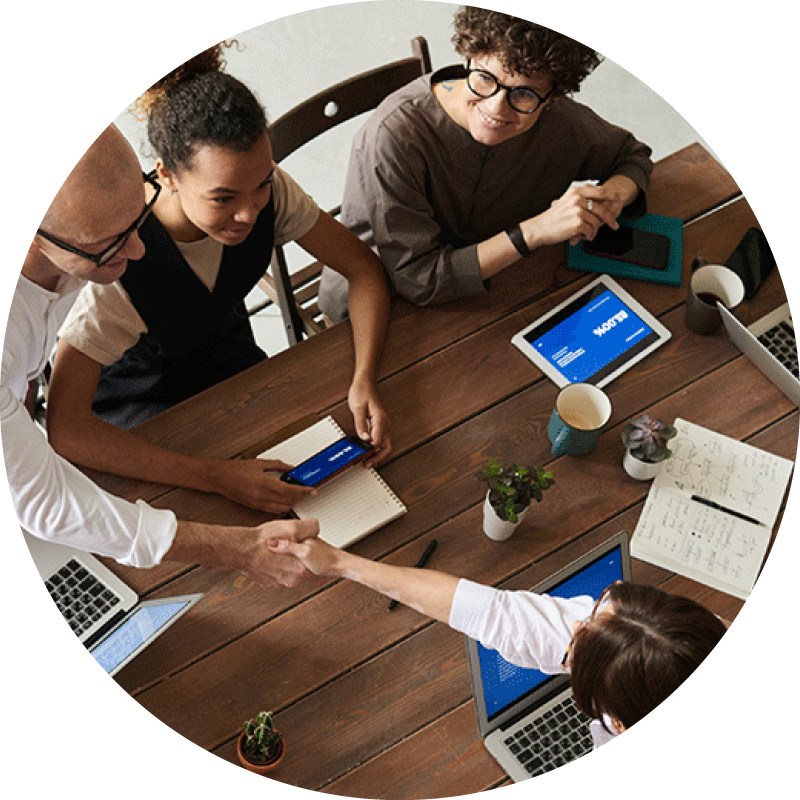 Overhead view of a group of people working at a table, while a man and a woman stand to shake hands