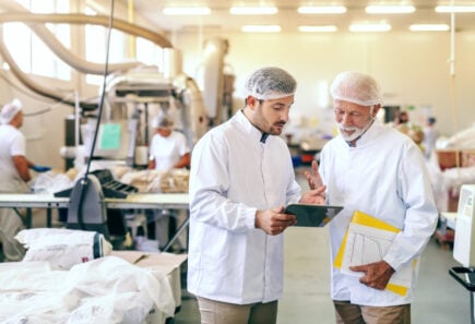 Two workers in sterile clothing inside a food manufacturing facility