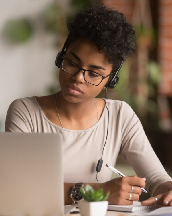 Student wearing headphones taking notes in front of a laptop