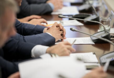 Politician’s hands folded over papers at his desk with a microphone