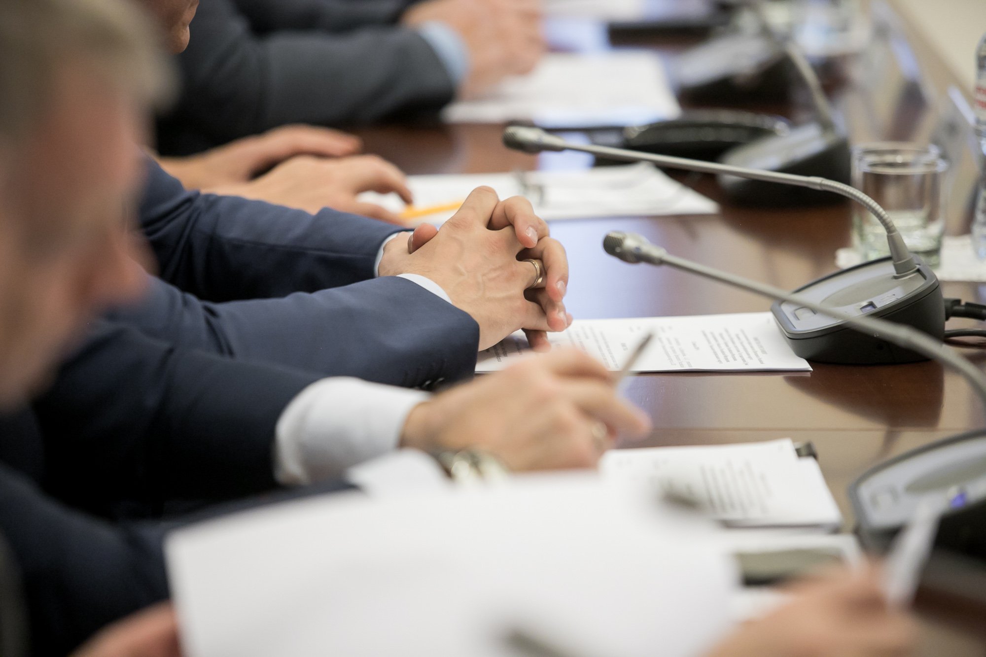 Politician’s hands folded over papers at his desk with a microphone