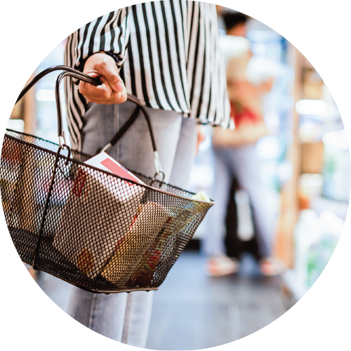 Grocery store scene with a person holding a shopping basket while browsing the refrigerated section