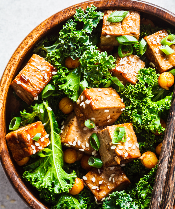 A wooden bowl filled with a meal of fried tofu, kale, and chickpeas