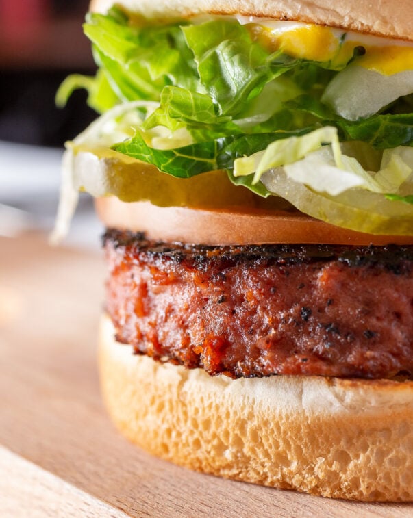 A closeup view of a plated plant-based burger with lettuce, tomatoes, and pickles