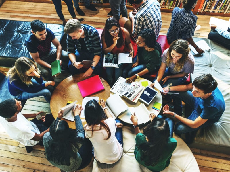 A group of students sitting around a table, with books open, studying, smiling, and working together.