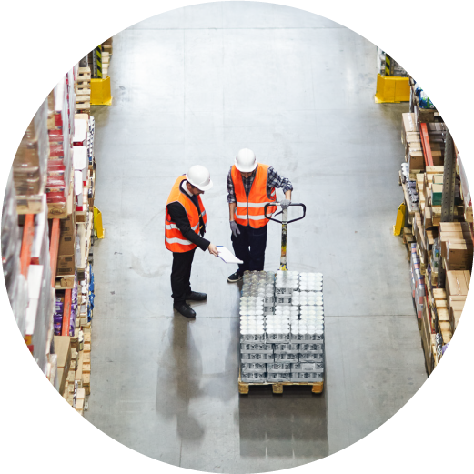 Two workers discuss packed goods pushing a pallet inside a warehouse