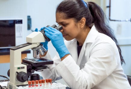 Scientist looking through a microscope, wearing blue gloves