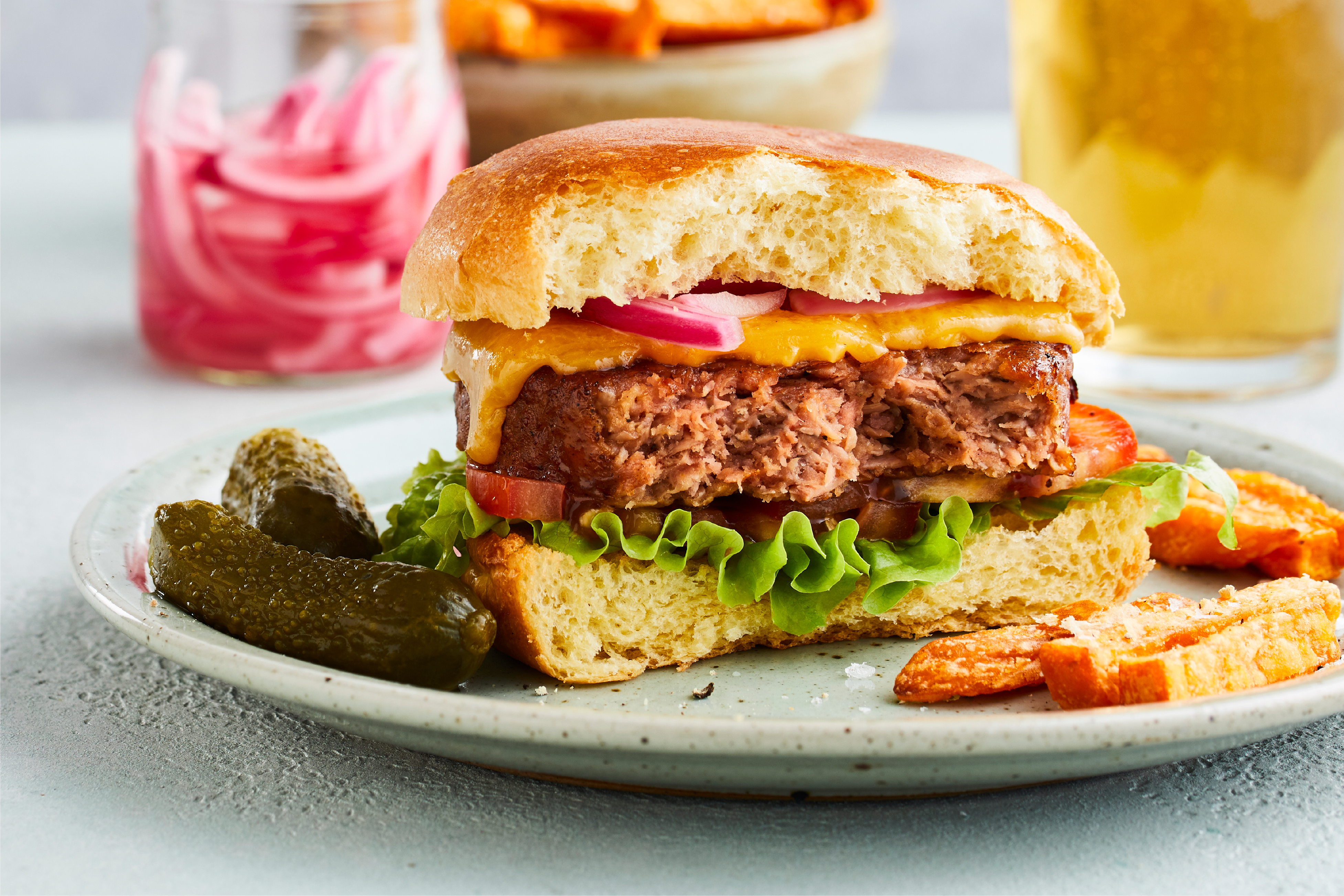 Half eaten plant-based cheeseburger with fries and pickles