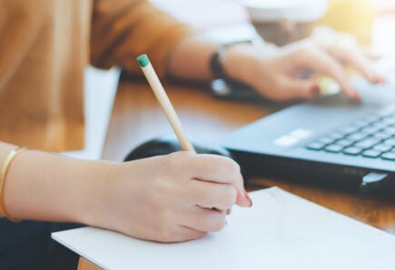 Woman taking notes while typing on a laptop