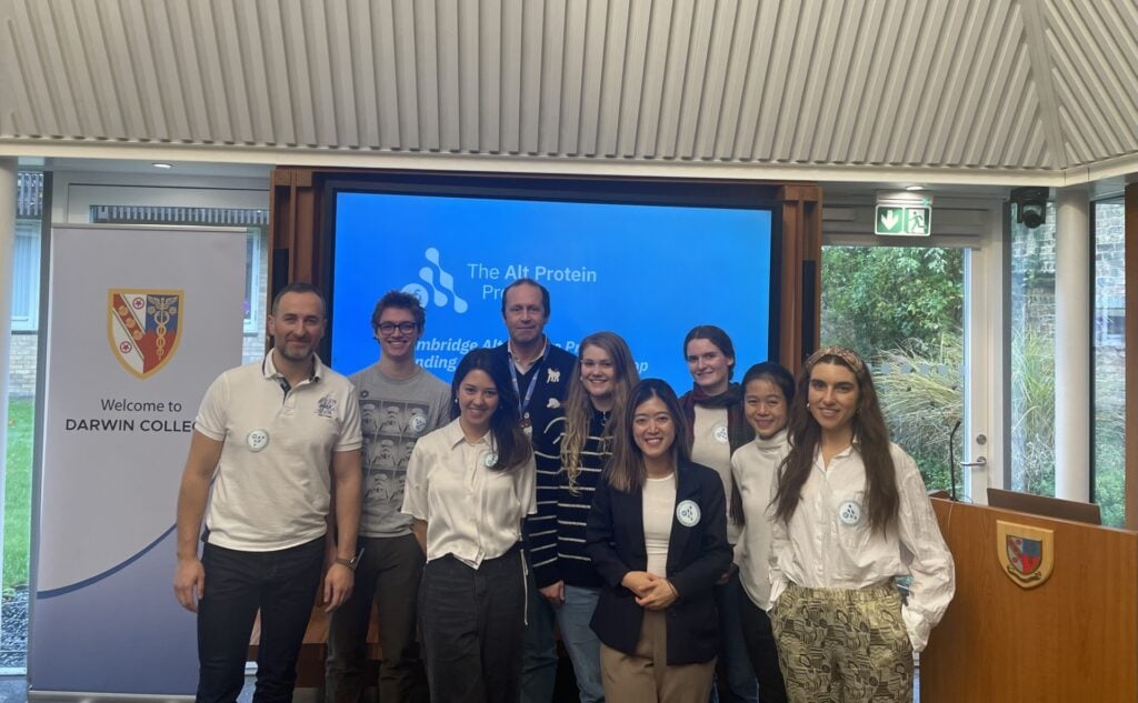 Nine students posing before a slide presentation