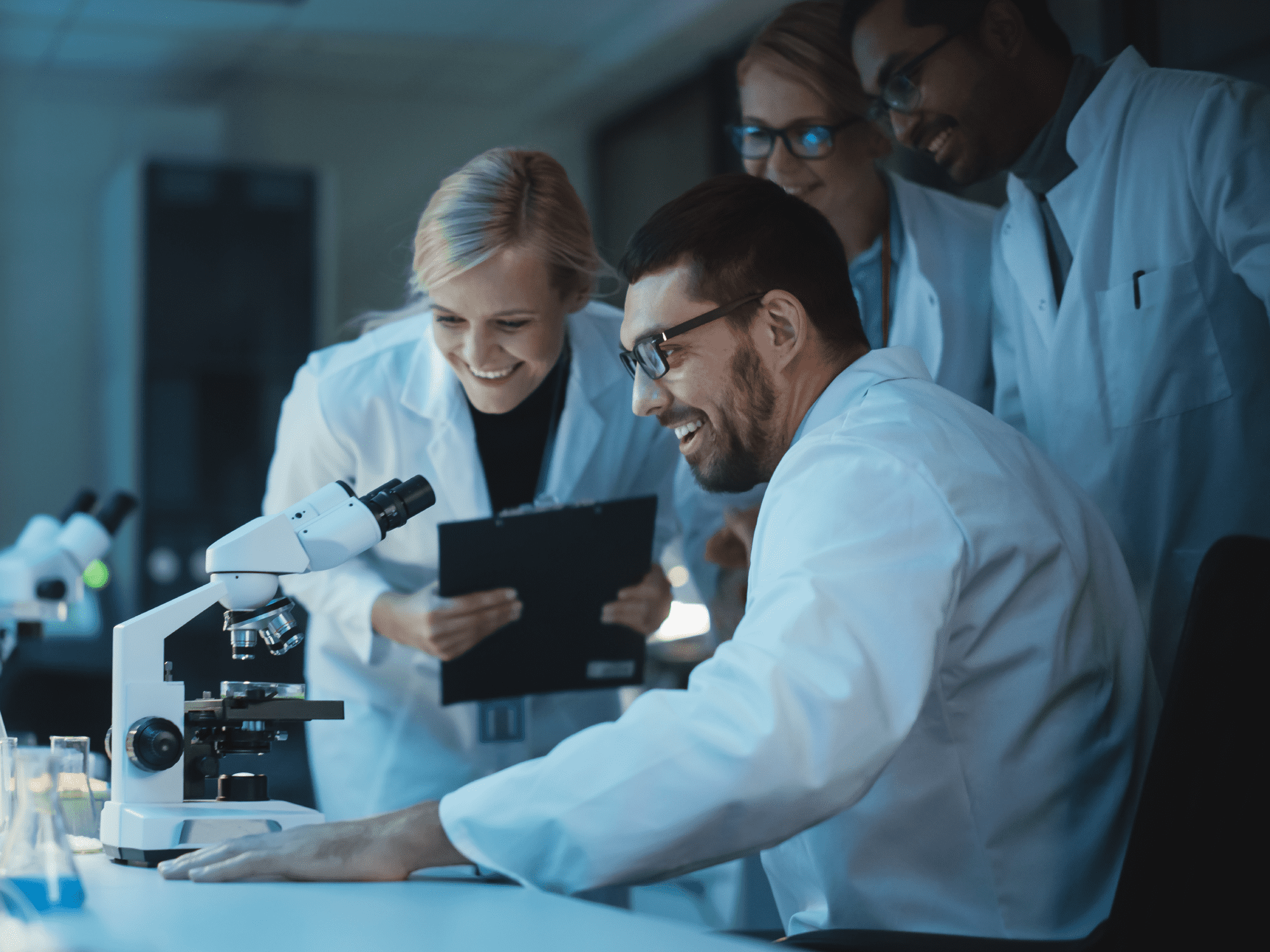 Four scientists look into a microscope in a lab