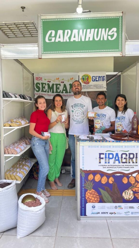 Four people standing at a Semear project display featuring seeds cultivated by farming communities in Pernambuco.