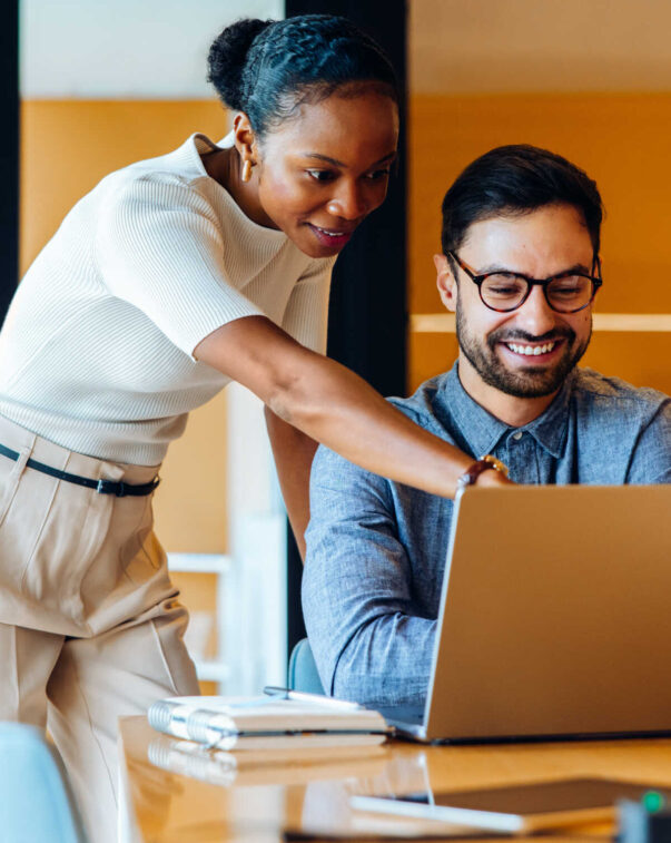 Coworkers collaborating and smiling while using laptop