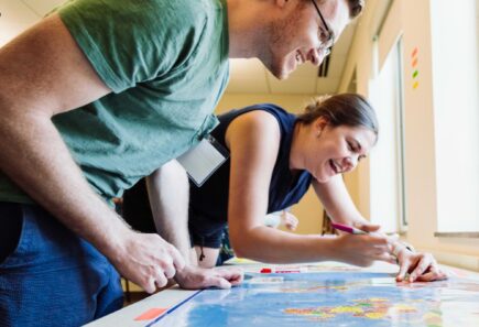 Two smiling people leaning over a table and writing