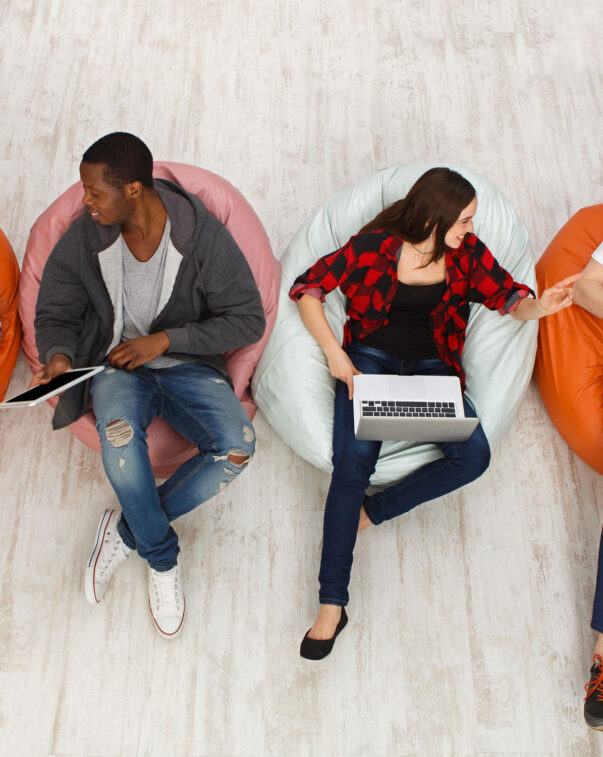 Students sitting in bean bag chairs talking and working on laptops