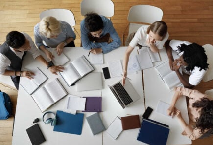 A group of people at a table with notebooks and laptops