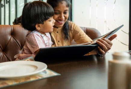 A South Asian mother and child look at a restaurant menu together