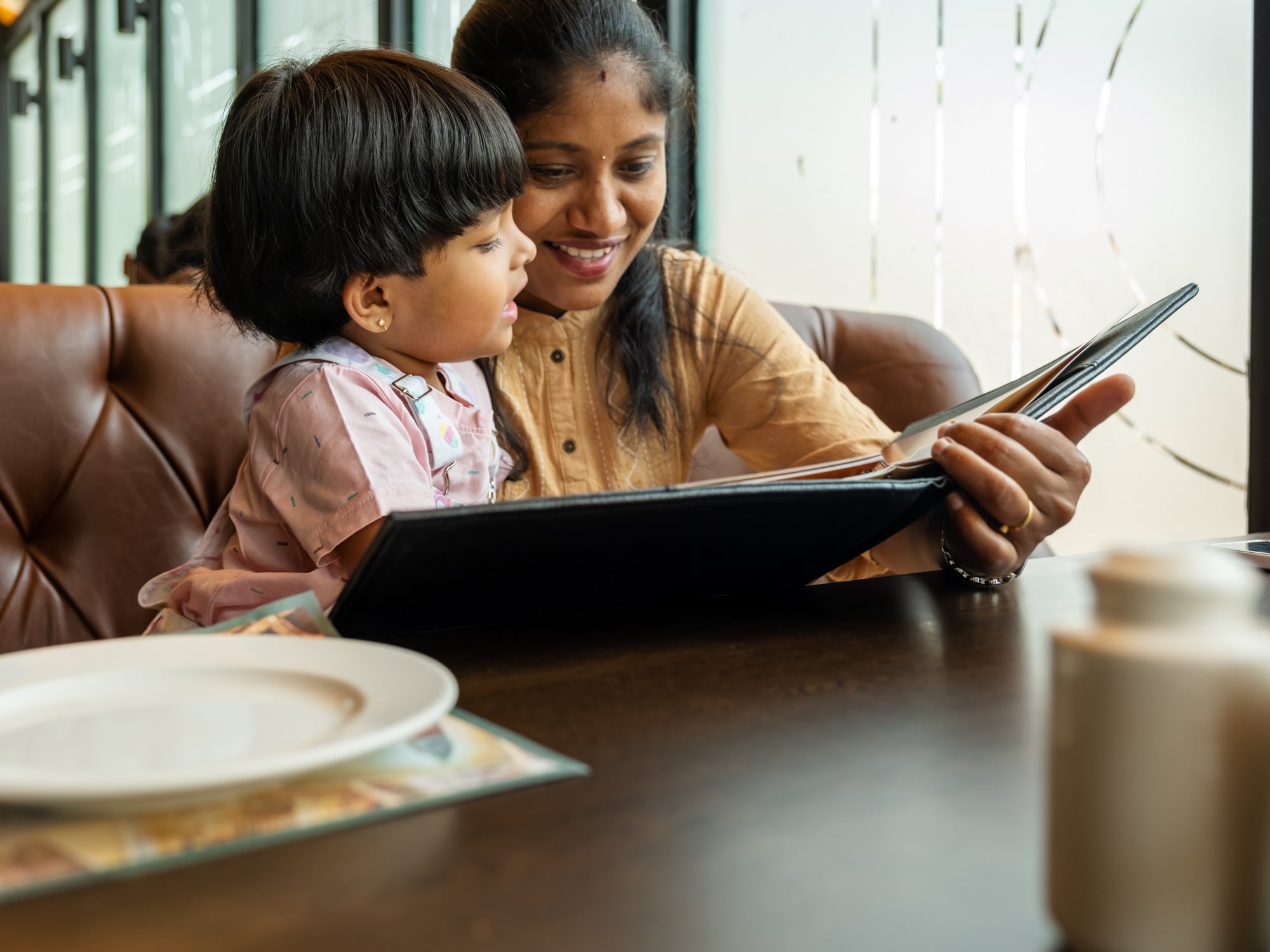 A south asian mother and child look at a restaurant menu together